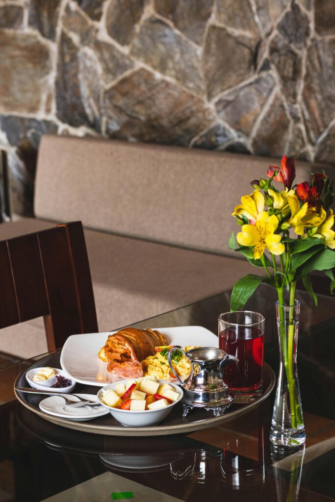 A stylish breakfast setup including croissants, fruits, and a beverage beside vibrant flowers indoors.